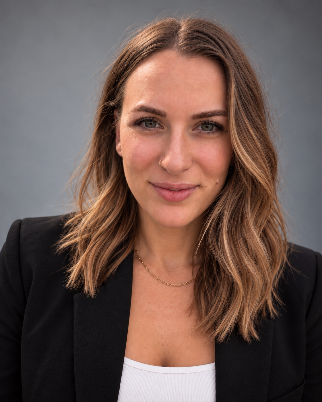 Portrait of a smiling woman with shoulder-length brown hair, wearing a black blazer and white top against a gray background