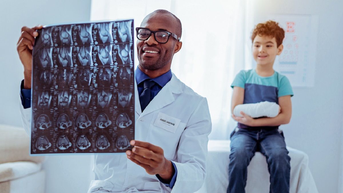 Doctor showing brain scans to a seated child in a clinic waiting room.
