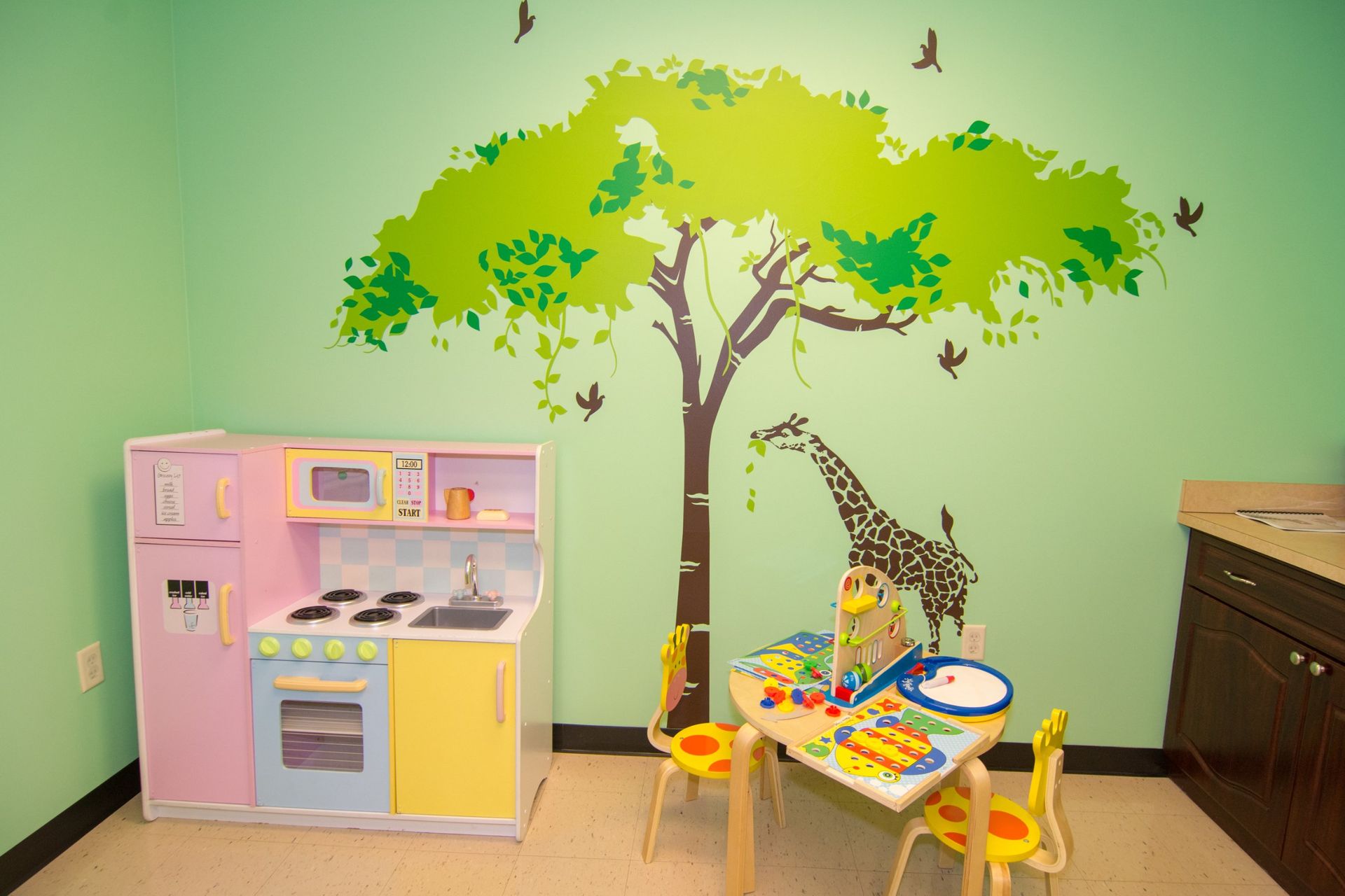 kitchen play set against a light green wall with a tree and giraffe sticker