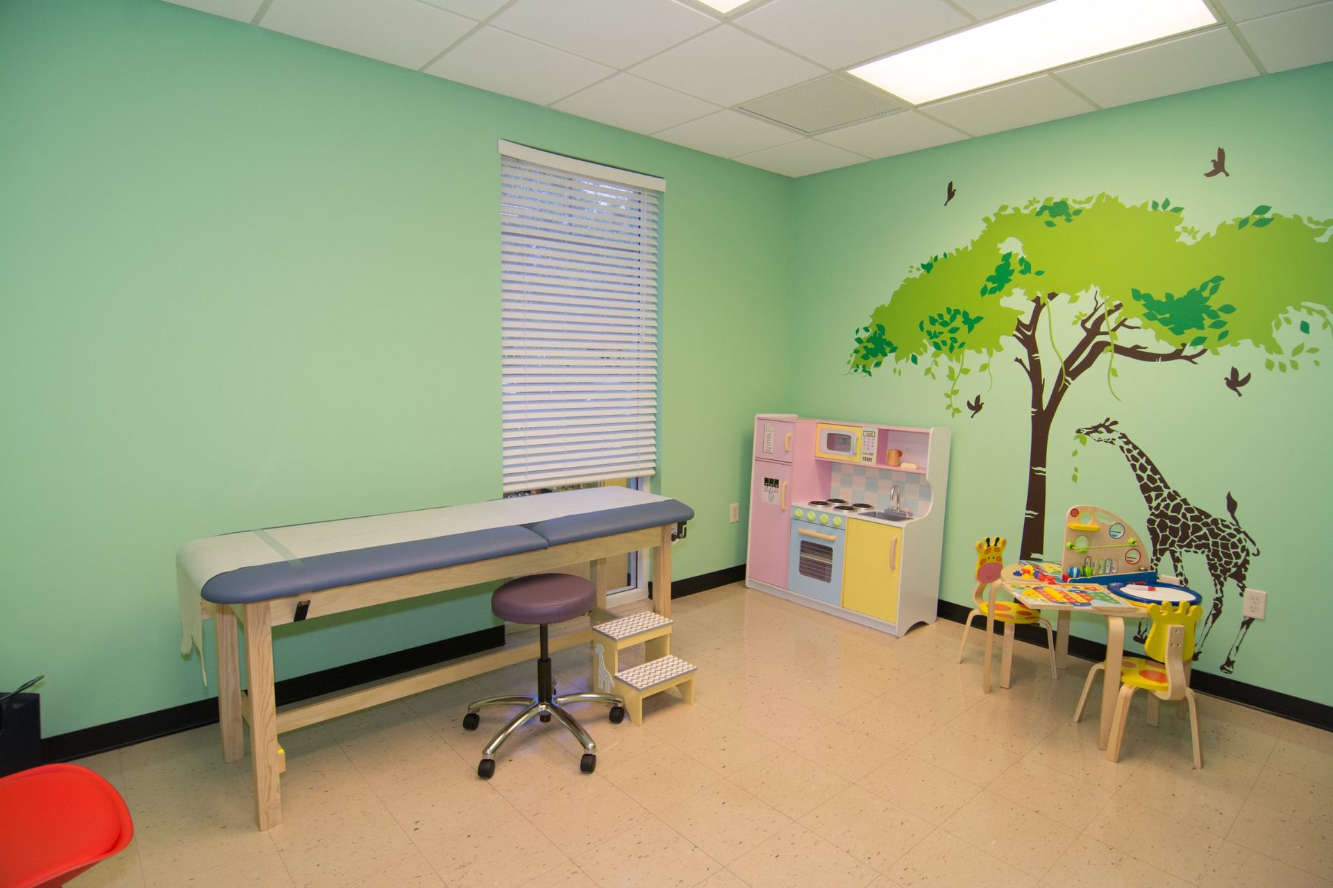 Photo of the consultation room with light green walls with a tree and giraffe sticker, showing the examination bed