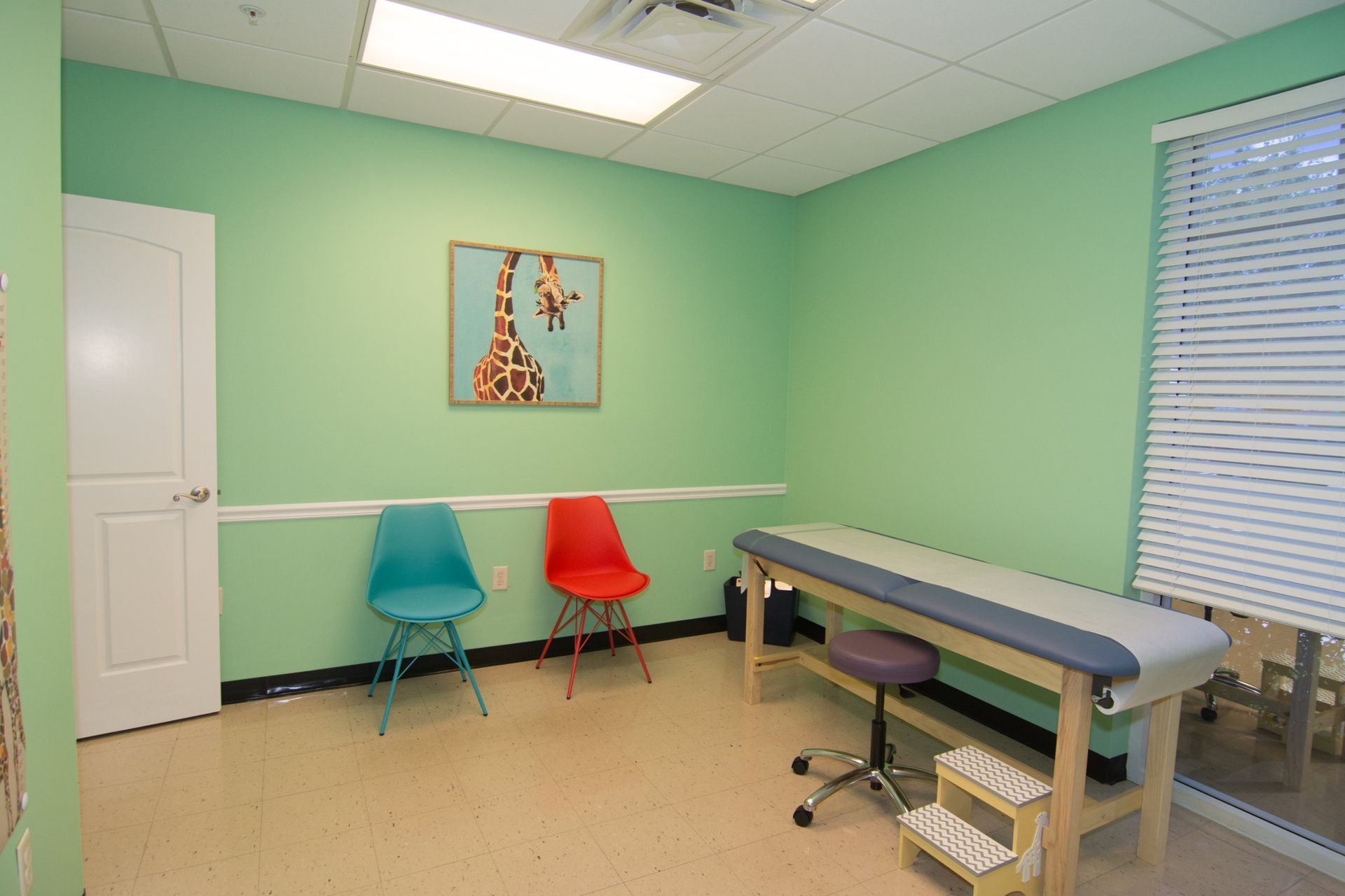 photo of the consultation room. red and blue chairs below a painting of a zebra hanging from the light green wall
