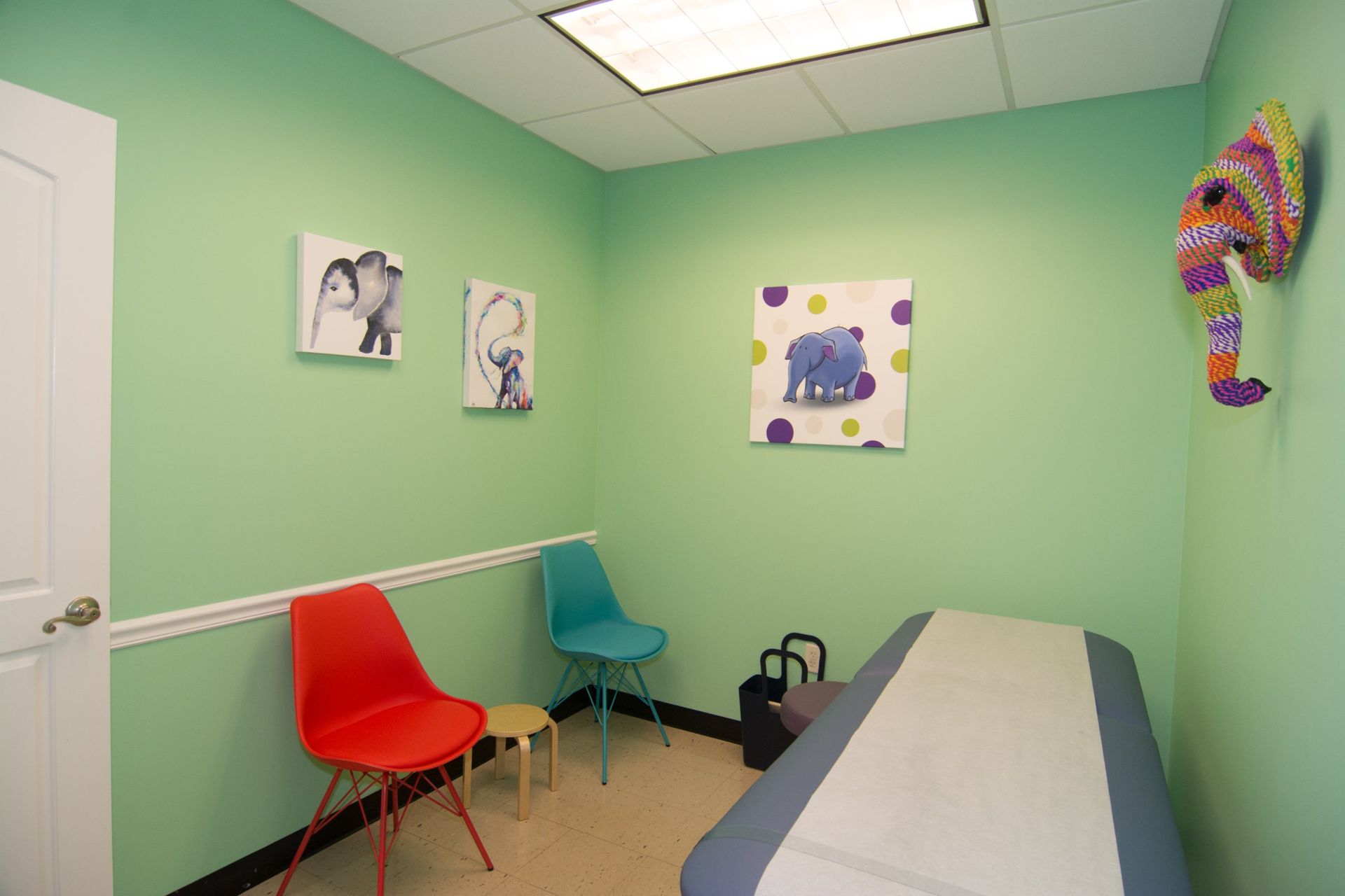 photo of the consultation room showing red and blue chairs against the wall, a bed on the opposite direction