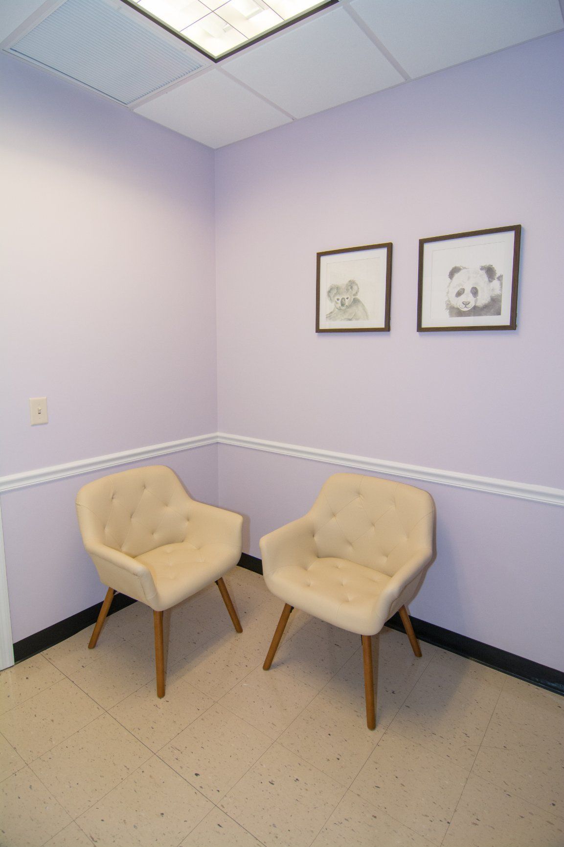 two beige colored chairs against the wall, light purple background and two framed pencil drawings of a koala and panda