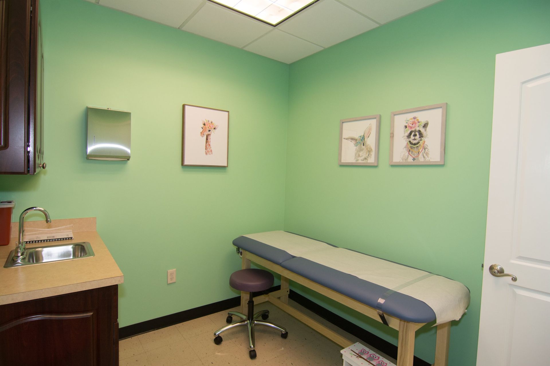photo of the consultation room with light green walls, one bed against the wall beside the white door on the right