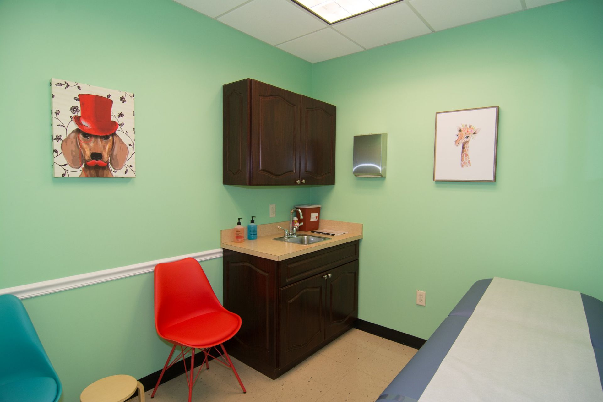 Photo of the consultation room with a bed, red and blue chair beside the sink and closet