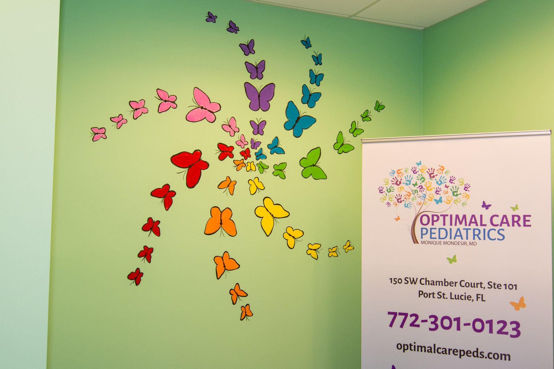 Spiralling butterflies stickers on a green wall, beside a tarp with Optimal Care Pediatrics logo