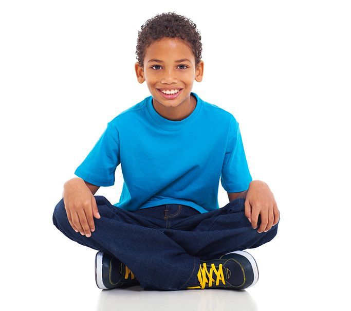 Young black boy wearing jeans and a blue shirt, sitting on the floor in an Indian sitting position