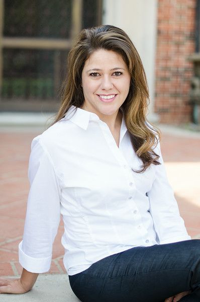 A woman in a white shirt and jeans is sitting on a brick sidewalk.