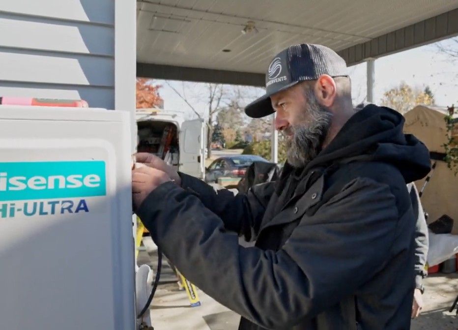 Un homme en veste noire travaille sur un appareil Hisense Hi-Ultra blanc à l'extérieur, sous un abri.