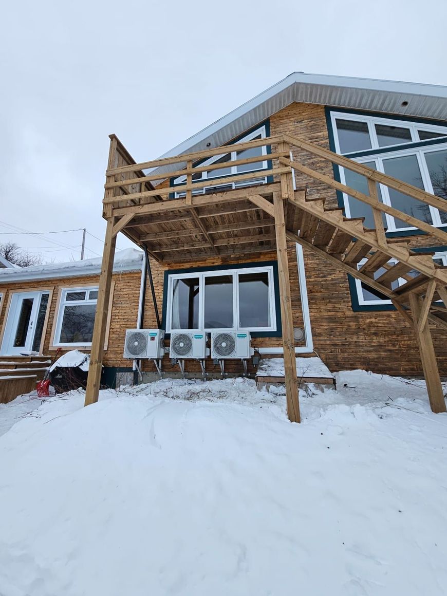 Bâtiment en bois enneigé de deux étages avec un escalier extérieur et un balcon, vu d'en bas.