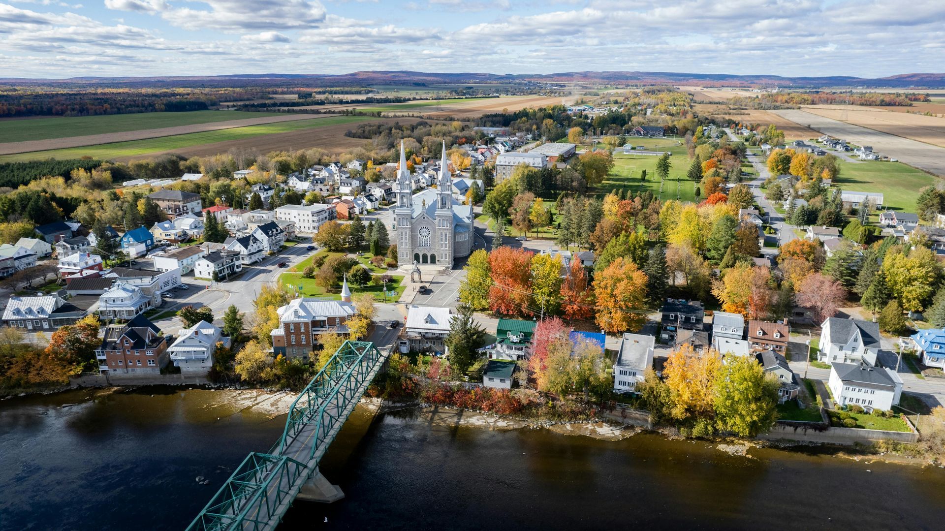 Vue aérienne d'une ville riveraine avec des arbres d'automne, un clocher et un pont sur l'eau