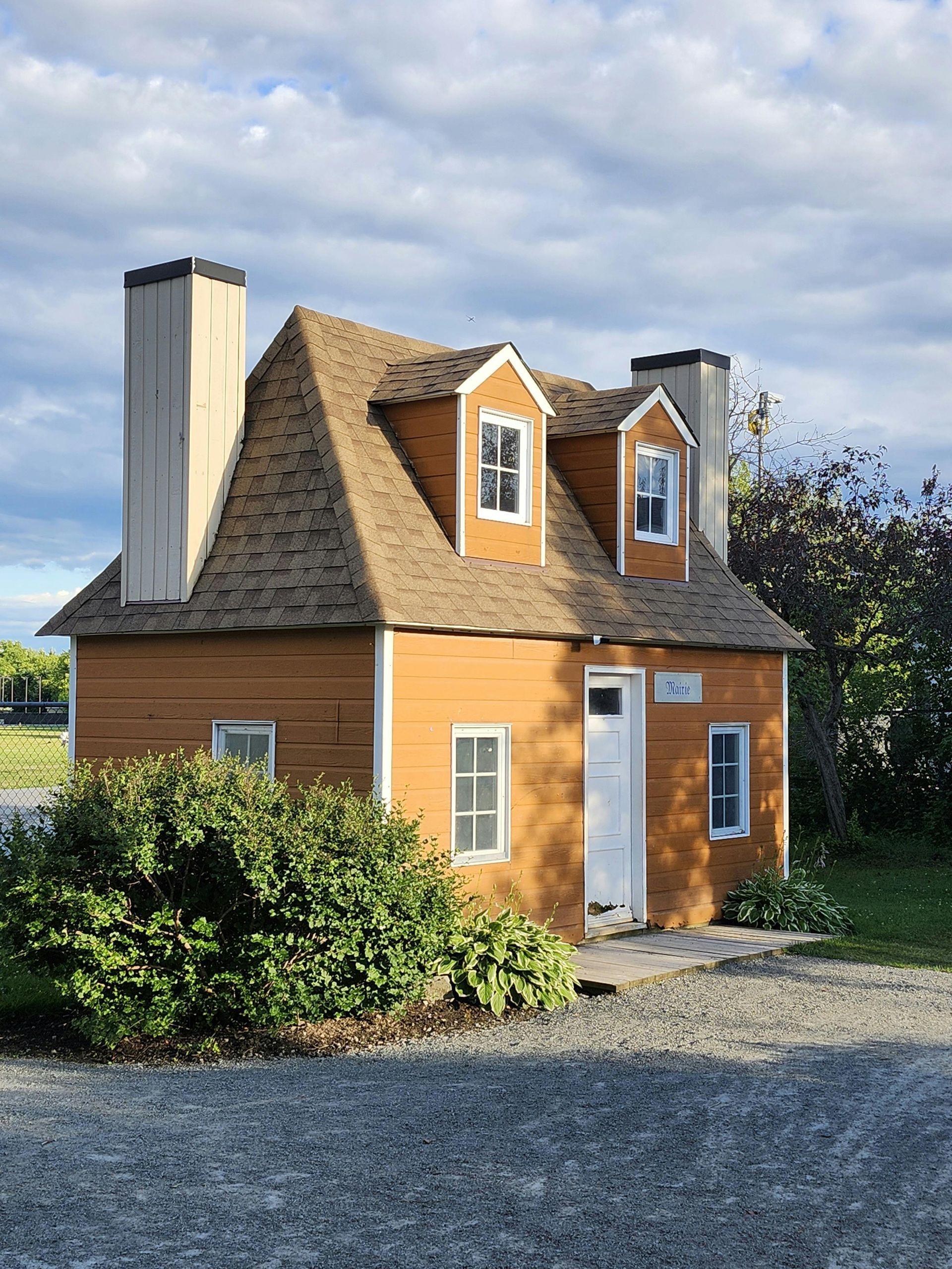 Petit chalet orange au toit pentu de bardeaux et aux cheminées blanches sous un ciel nuageux