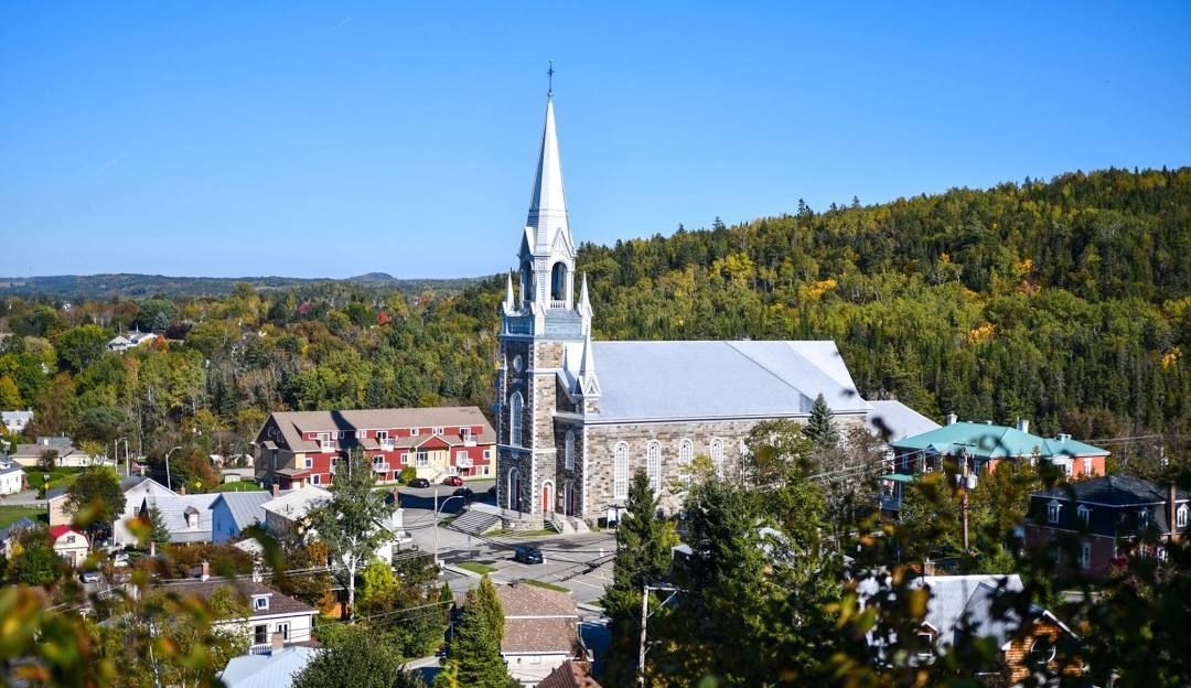 Le clocher d'une haute église se dresse au-dessus d'une petite ville et d'arbres, sous un ciel d'un bleu limpide.