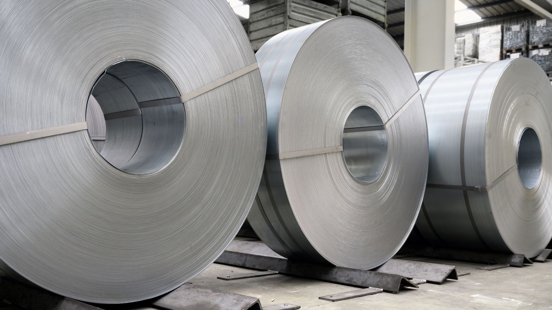 Tres grandes bobinas de acero apiladas en un entorno industrial.