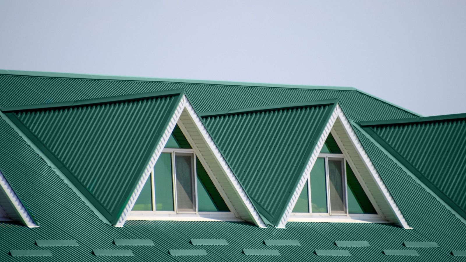 Techo de metal corrugado verde con buhardillas triangulares y molduras blancas.