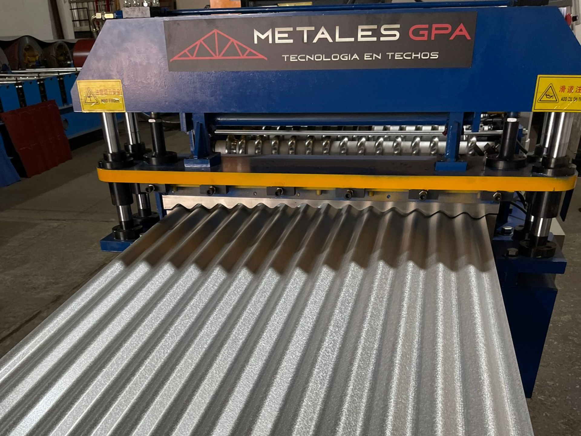 Chapa ondulada siendo formada por una máquina industrial de color azul; logo 