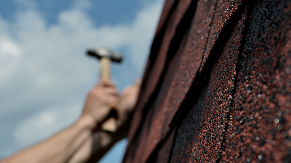 A person is holding a hammer on a roof.