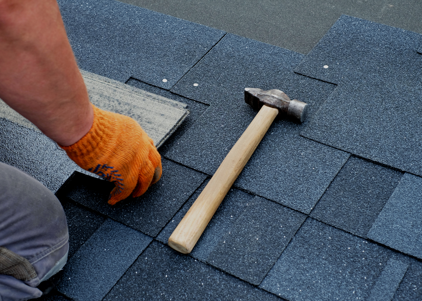 A man is installing shingles on a roof with a hammer.