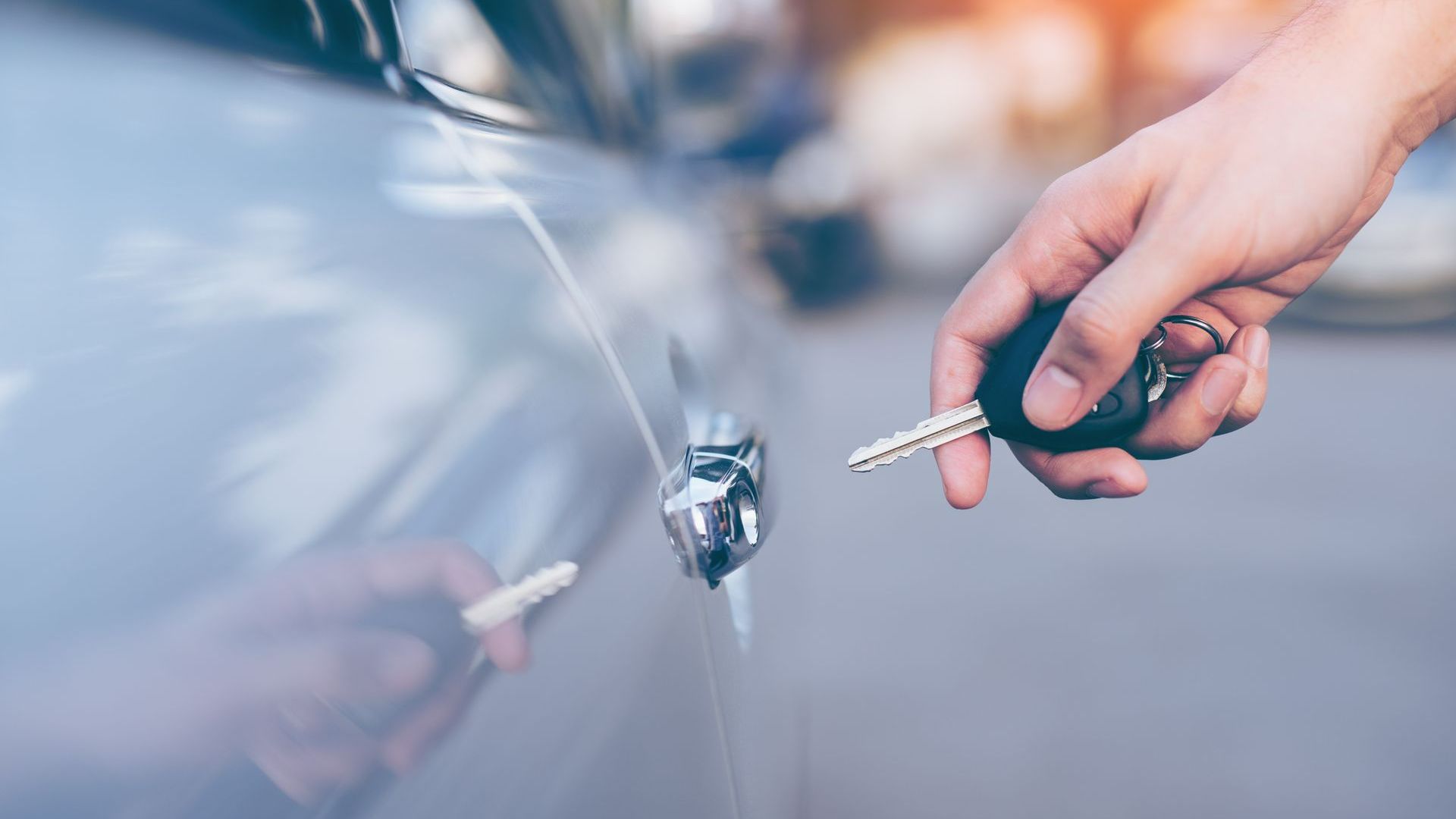 A Person Is Holding a Car Key in Front of A Car | Westminster, CO | M.L. Locksmith A Person Is Holding a Car Key in Front of A Car | Westminster, CO | M.L. Locksmith
