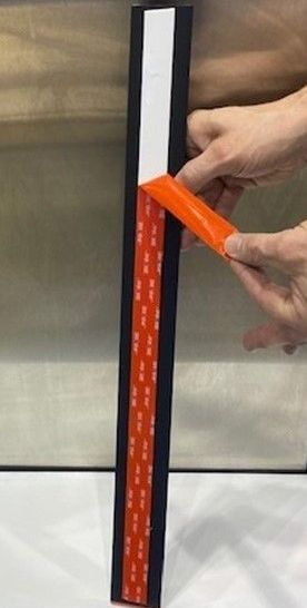 Hands peeling orange adhesive backing from a black and white strip with red adhesive on it.