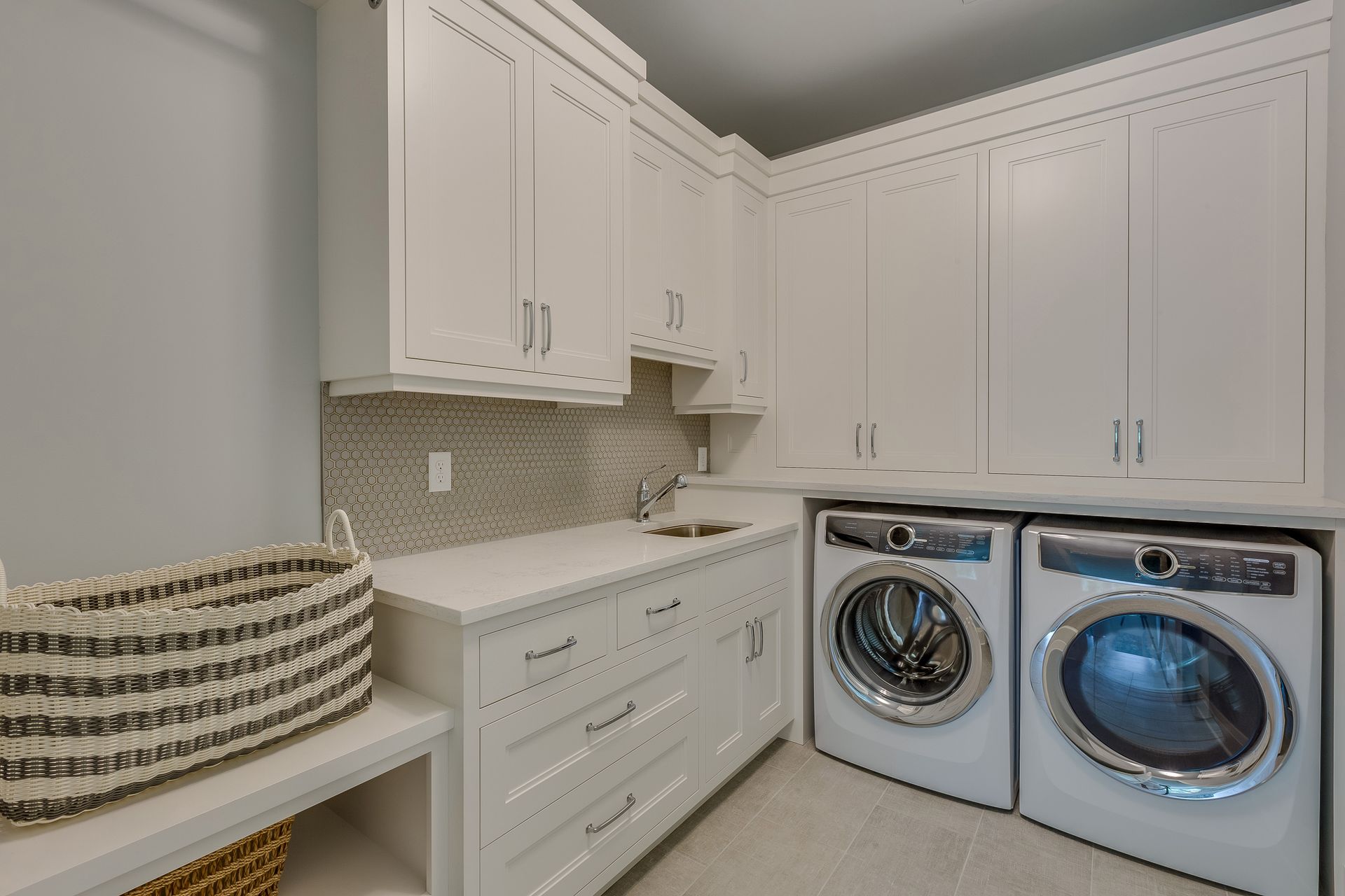White laundry room with cabinets, a sink, and a washer/dryer. A basket sits on a shelf.