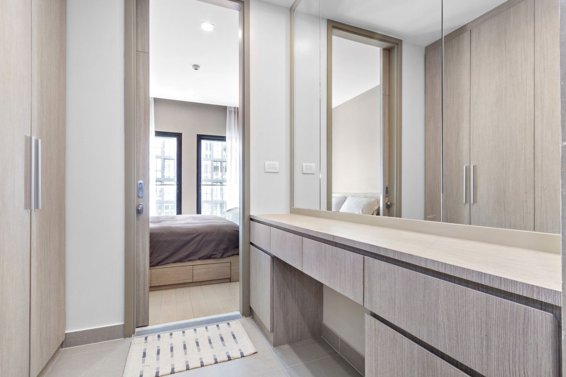 A dressing room with a vanity and walk-in closet leads to a bedroom with a bed.