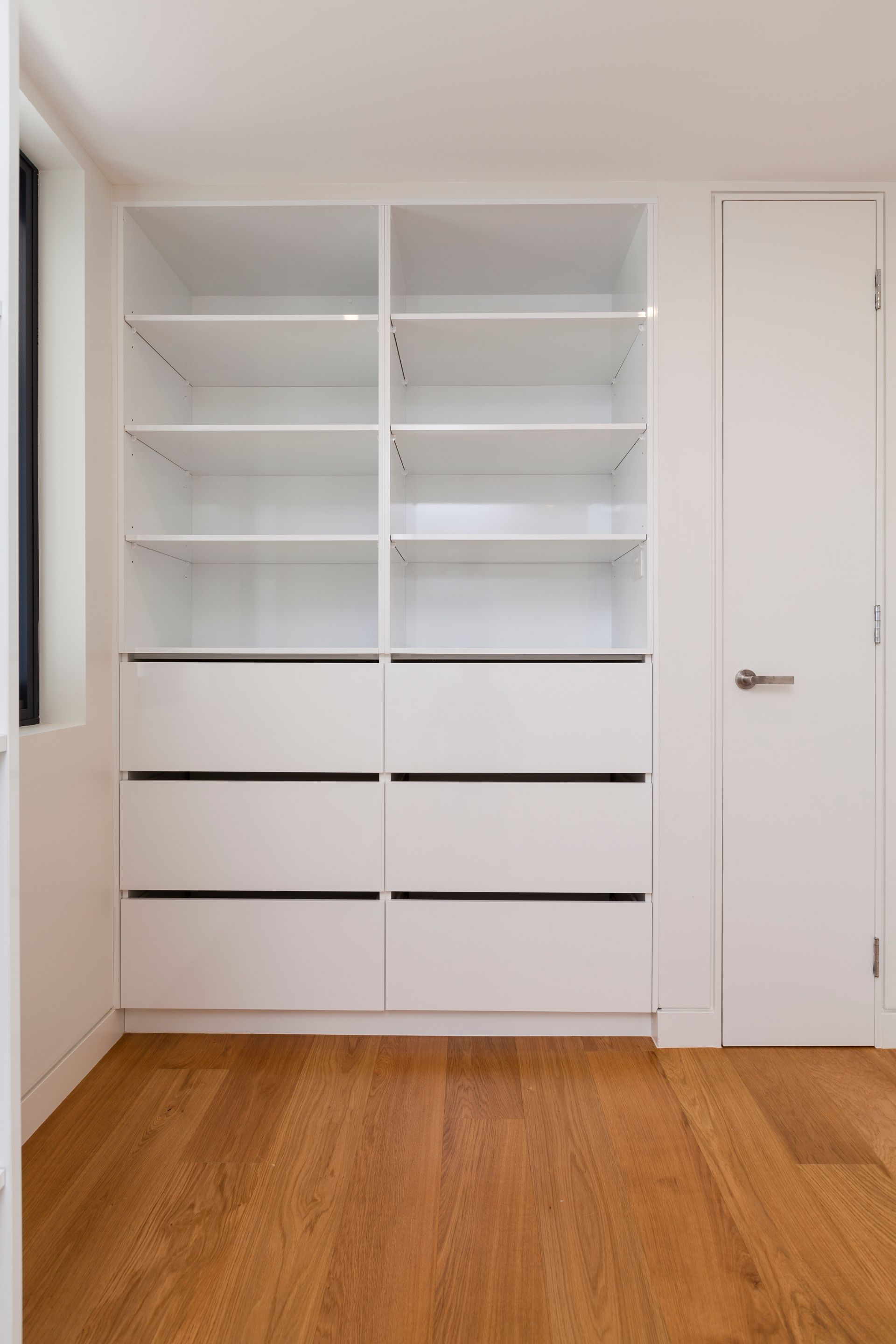 White built-in shelving unit with open shelves and drawers, next to a door, and wooden floor.