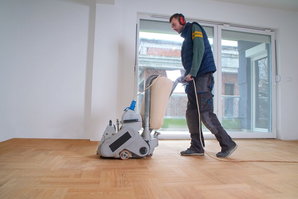 A Man is Sanding a Wooden Floor With a Machine — Norwood Floor Sanding in Byron Bay, NSW