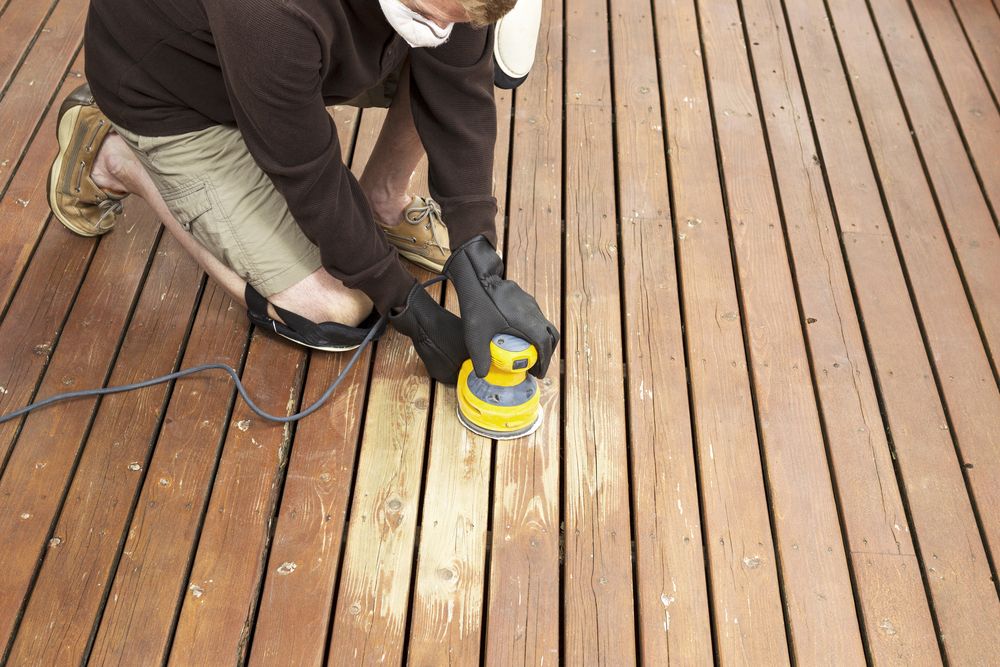 A Man is Sanding a Wooden Deck With a Sander — Norwood Floor Sanding in Ballina, NSW