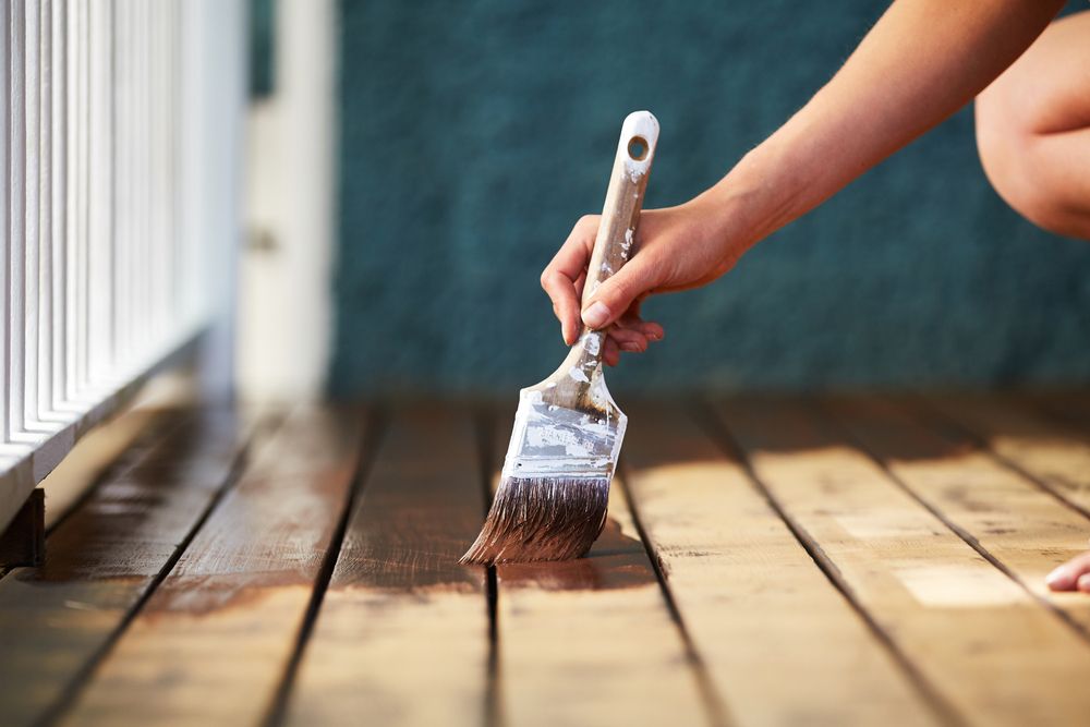 A Person is Painting a Wooden Deck With a Brush — Norwood Floor Sanding in Tweed Heads, NSW