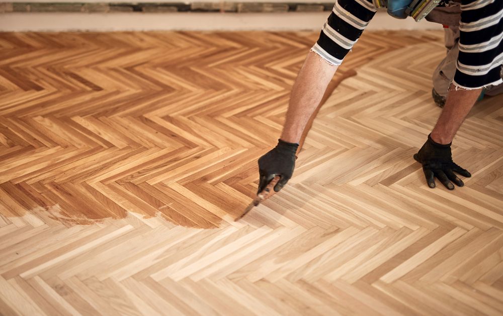 A Person is Painting a Wooden Floor With a Brush — Norwood Floor Sanding in Tweed Heads, NSW