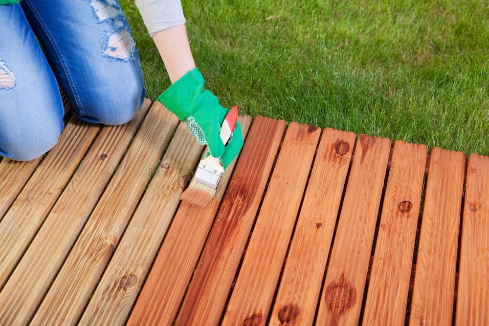 A Person is Painting a Wooden Deck With a Brush — Norwood Floor Sanding in Byron Bay, NSW