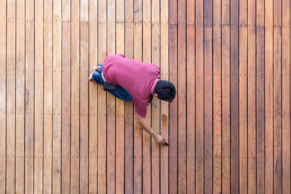 A Man is Painting a Wooden Deck With a Brush — Norwood Floor Sanding in Mullumbimby, NSW