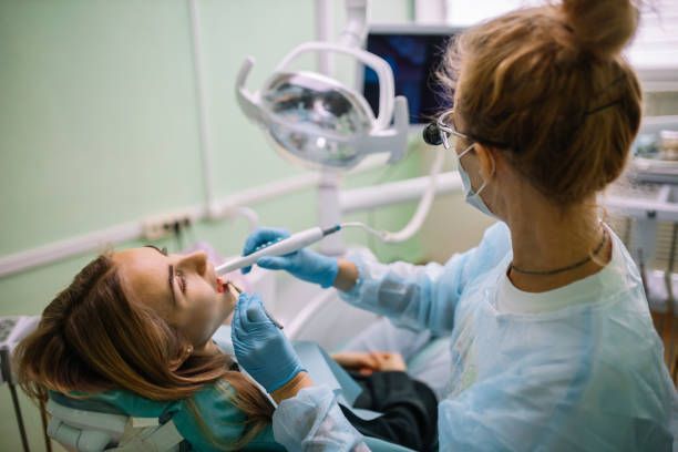 A female patient sitting in a chair with her mouth open as an emergency dentist conduct examination.
