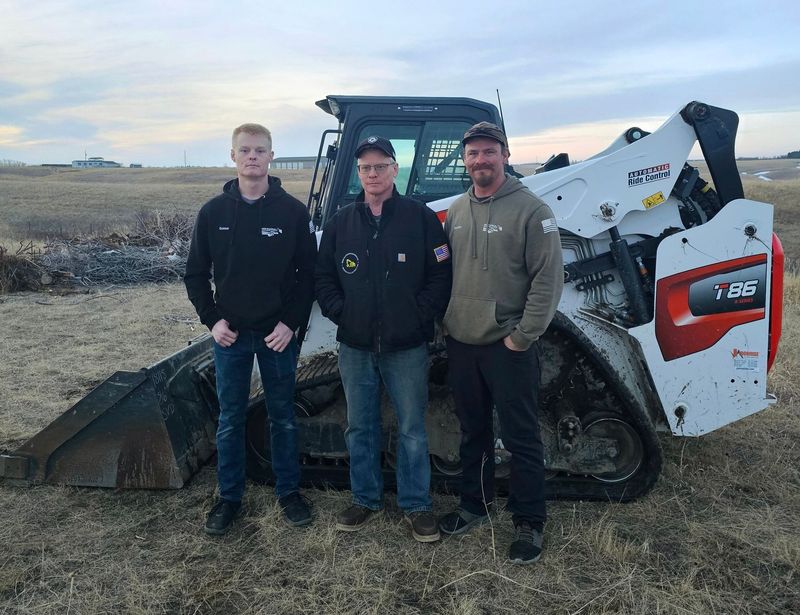 Three men are standing in front of a bulldozer in a field.
