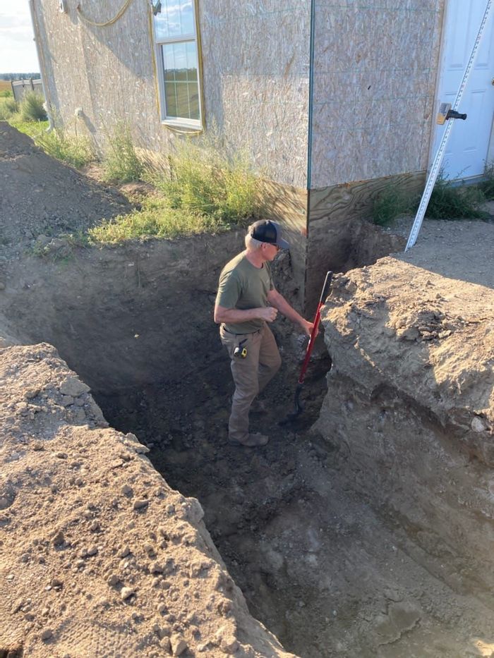 A man is digging a hole in the dirt in front of a house.