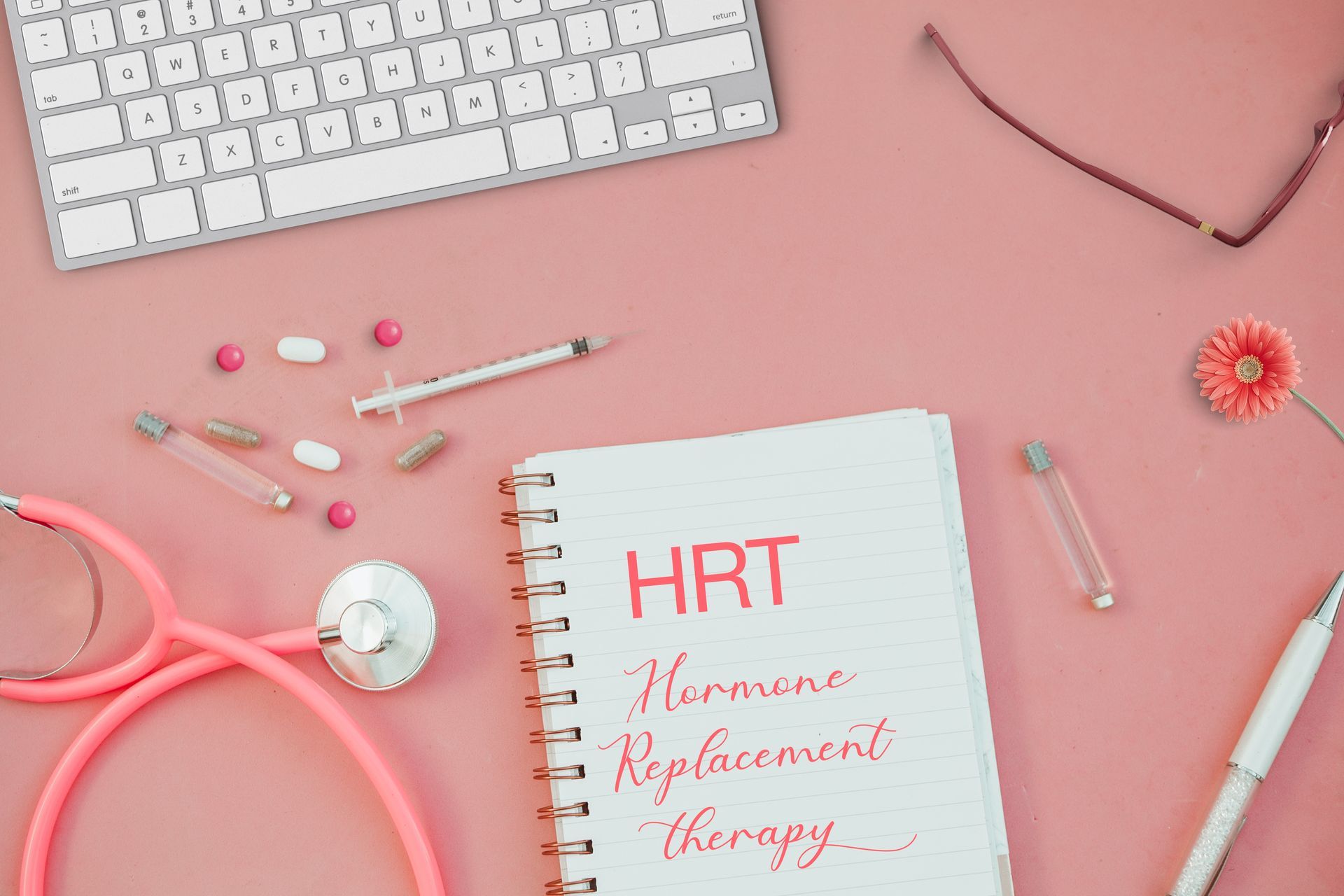A pink stethoscope is sitting next to a notebook that says hrt on it.