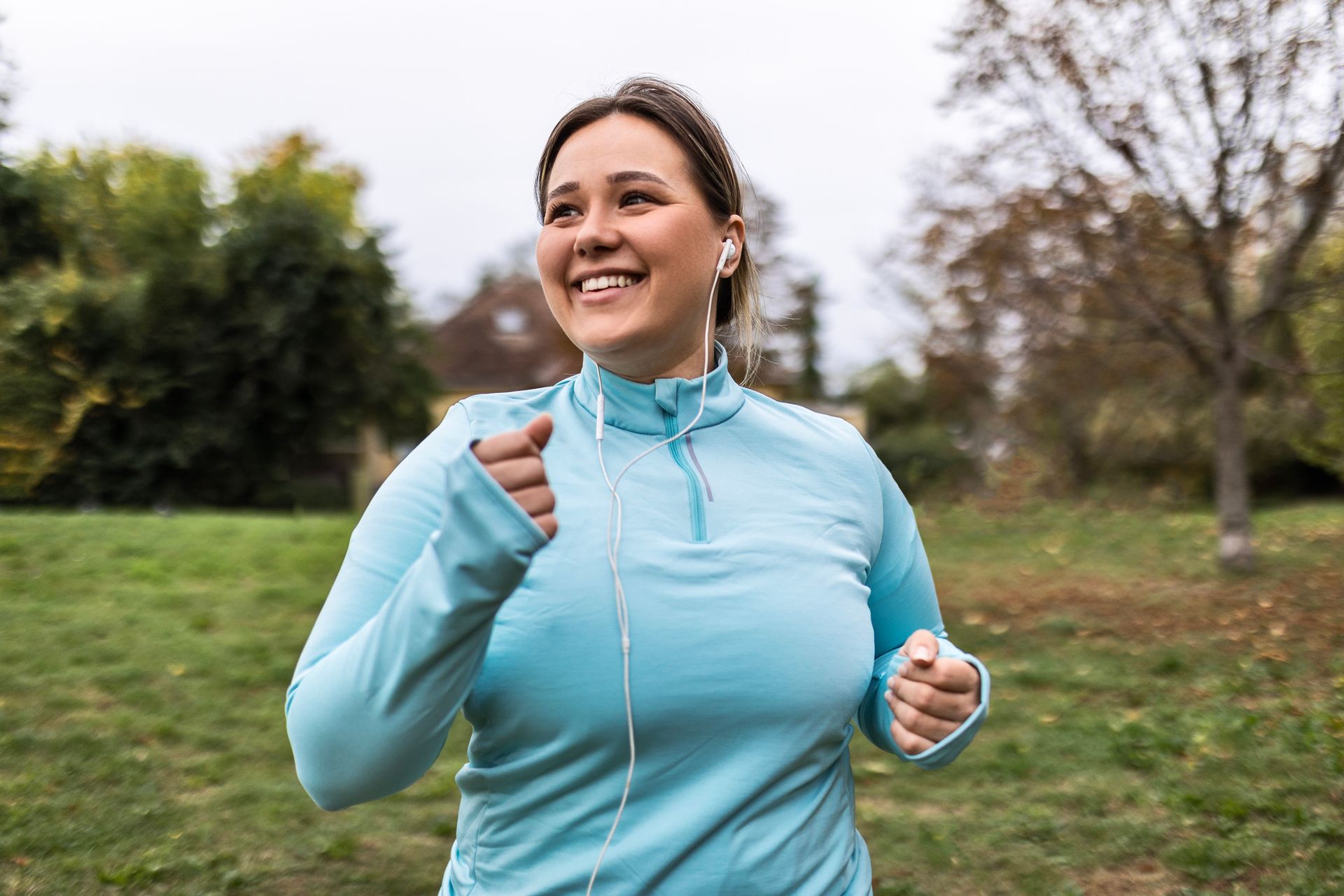 A woman is running in a park with headphones on.