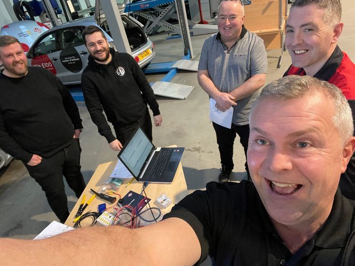 A group of men are standing around a table with a laptop on it.
