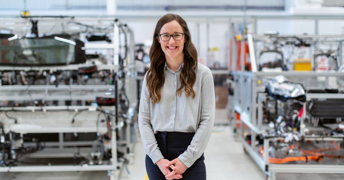 A woman is standing in a factory with a car in the background.