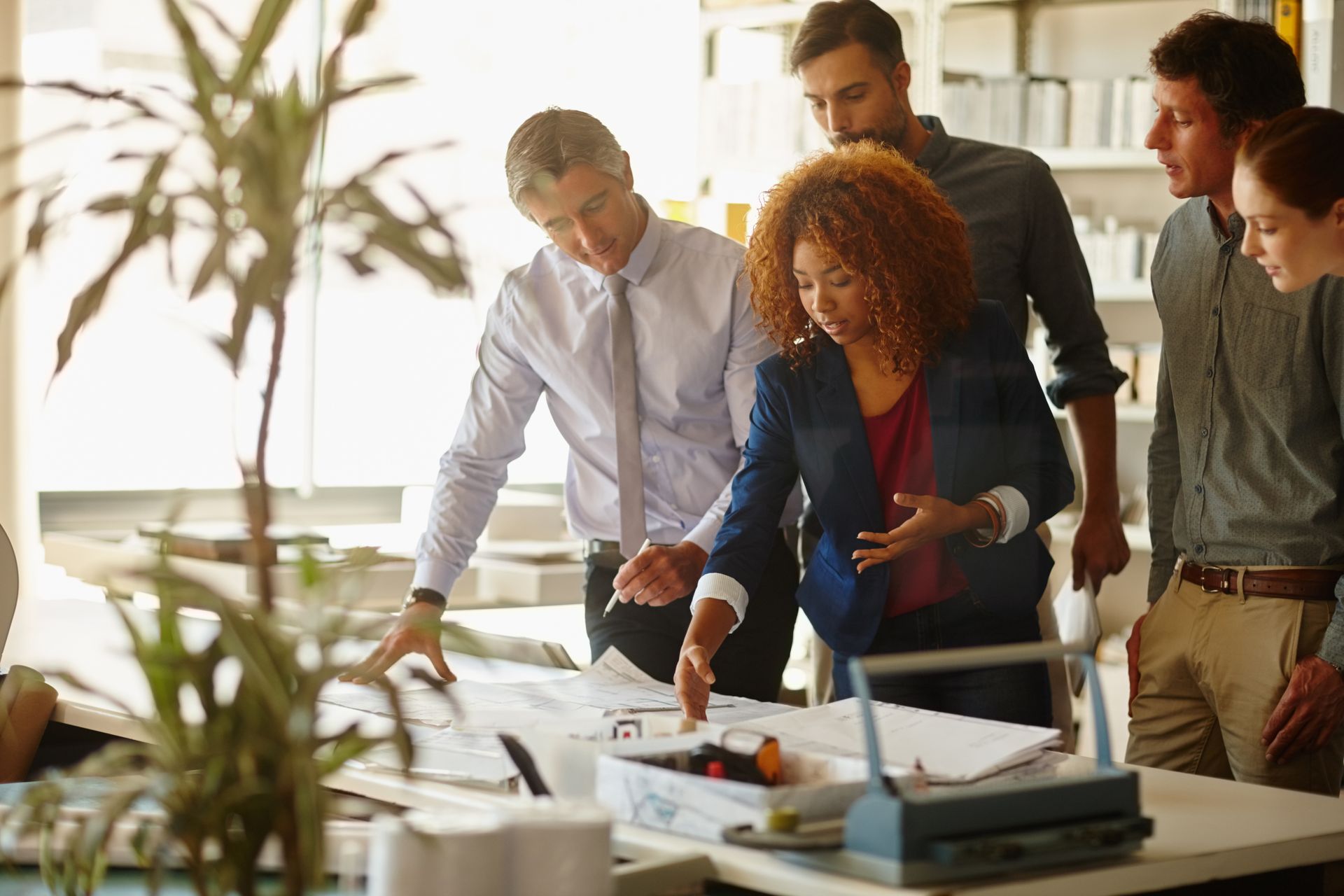 Colleagues gathered around a desk reviewing plans and documents in a bright office
