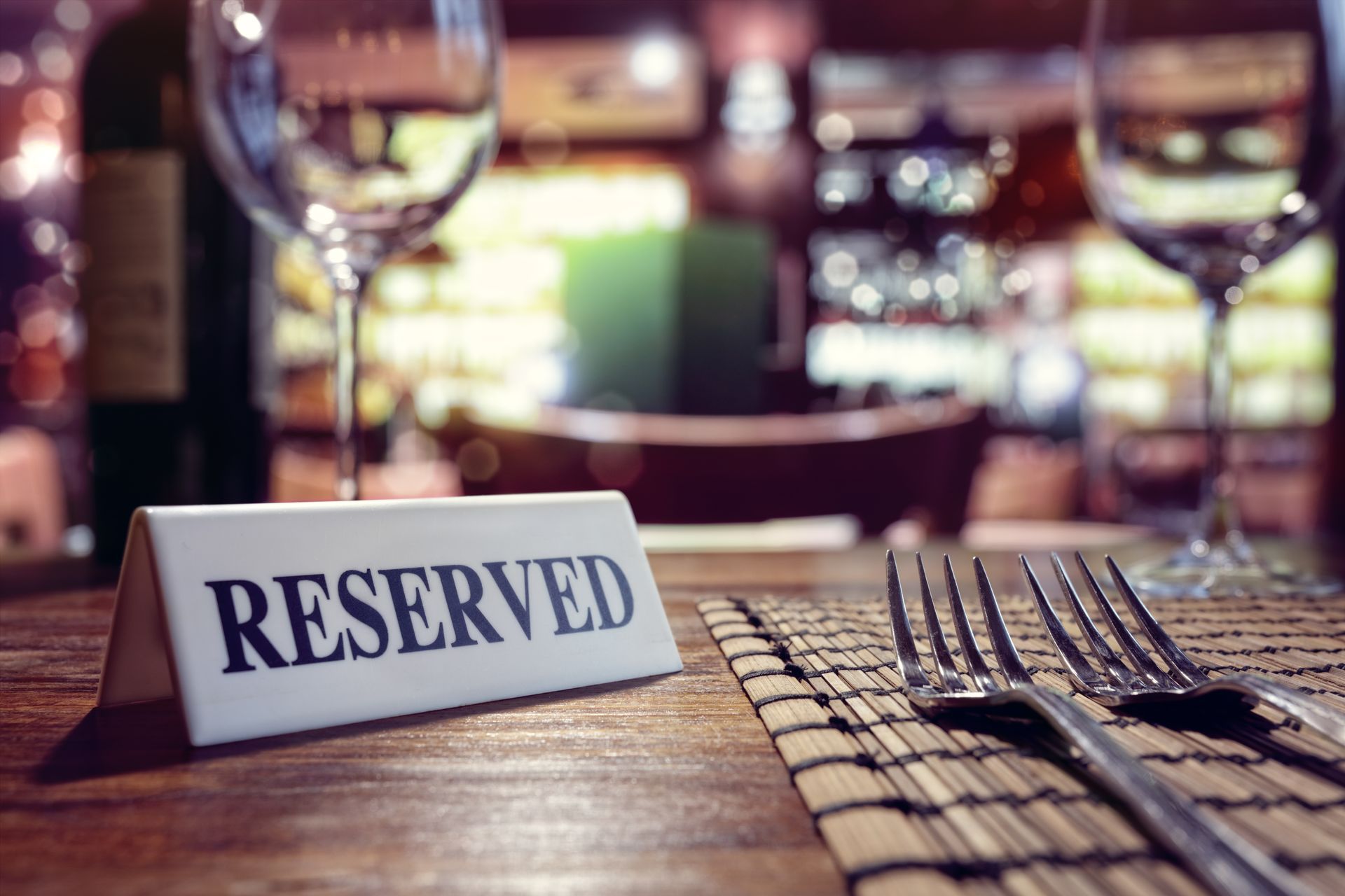 Reserved sign on a wooden restaurant table beside silverware and wine glasses, with a blurred dining background