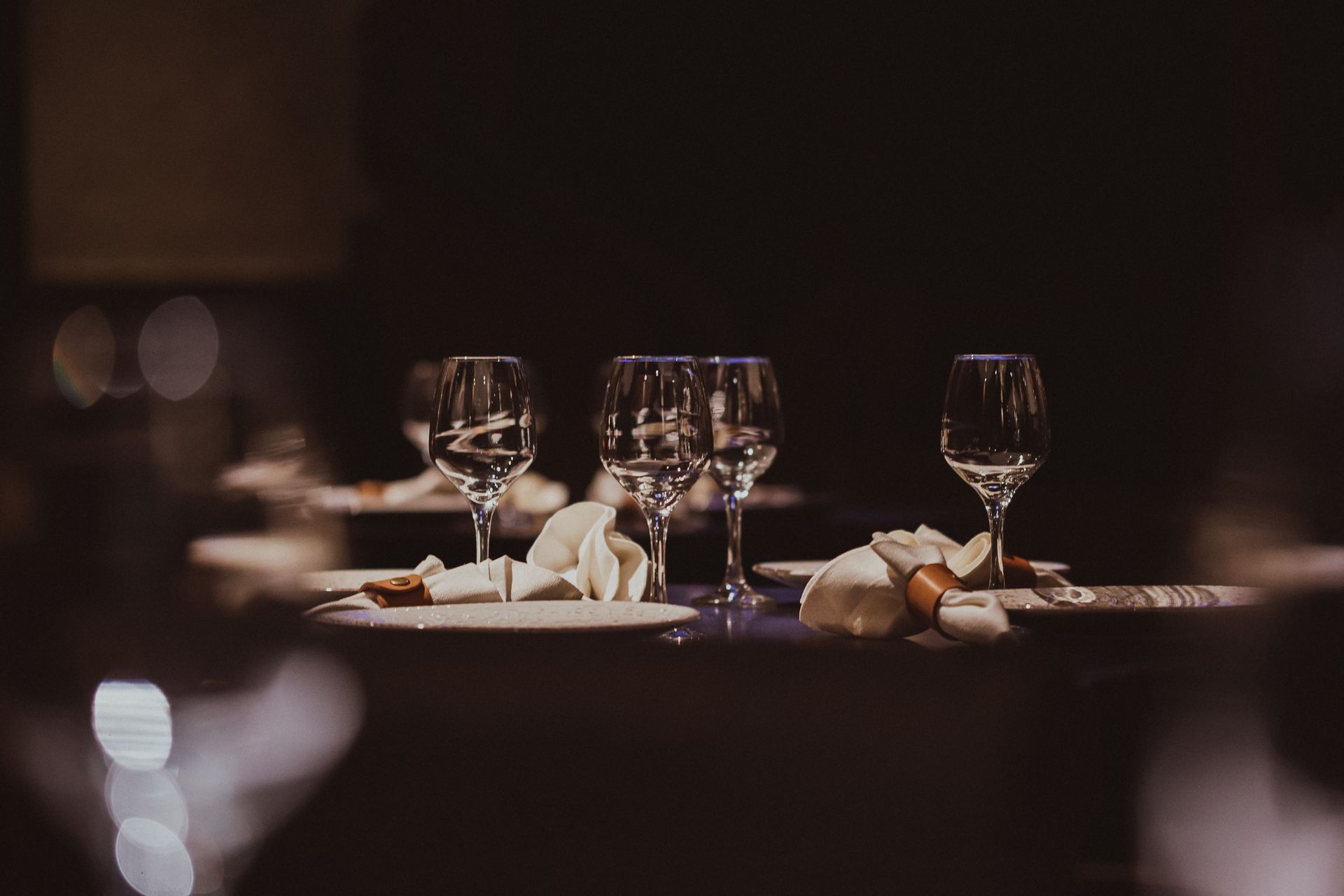 Elegant dining table set with wine glasses, bread rolls, and soft candlelit reflections in a dim restaurant