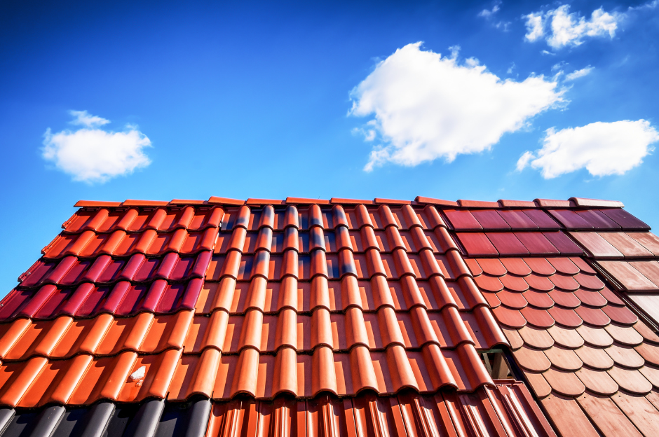 A roof with many different colored tiles against a blue sky with clouds