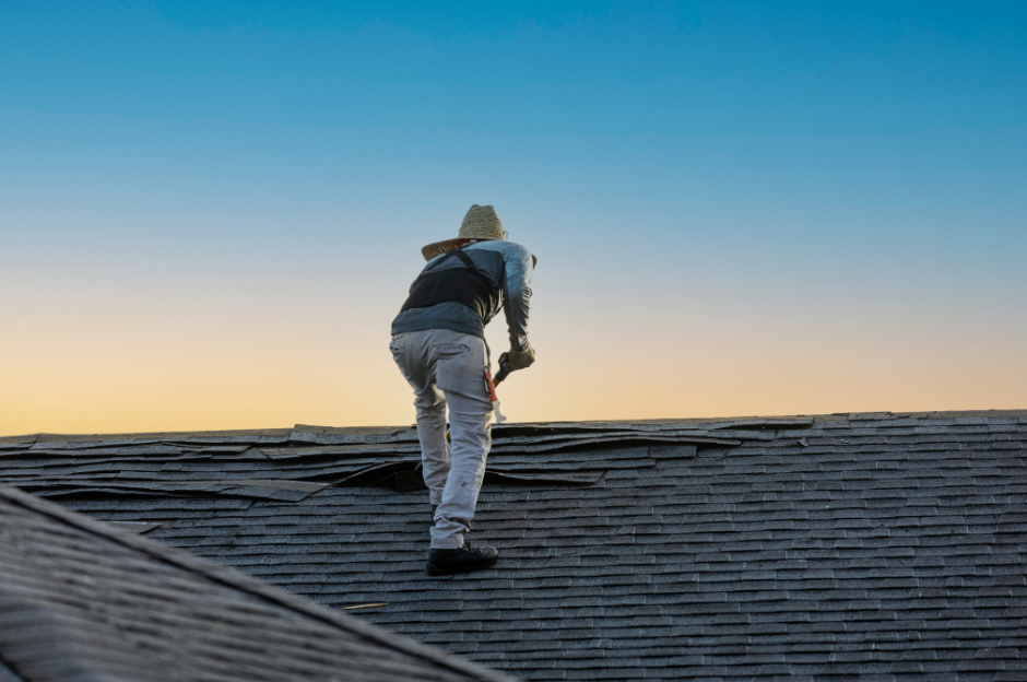 A man is standing on top of a roof holding a hammer.