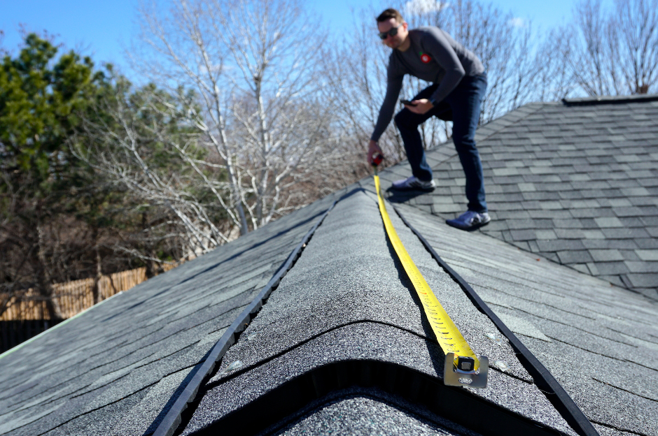 A man is measuring a roof with a tape measure.