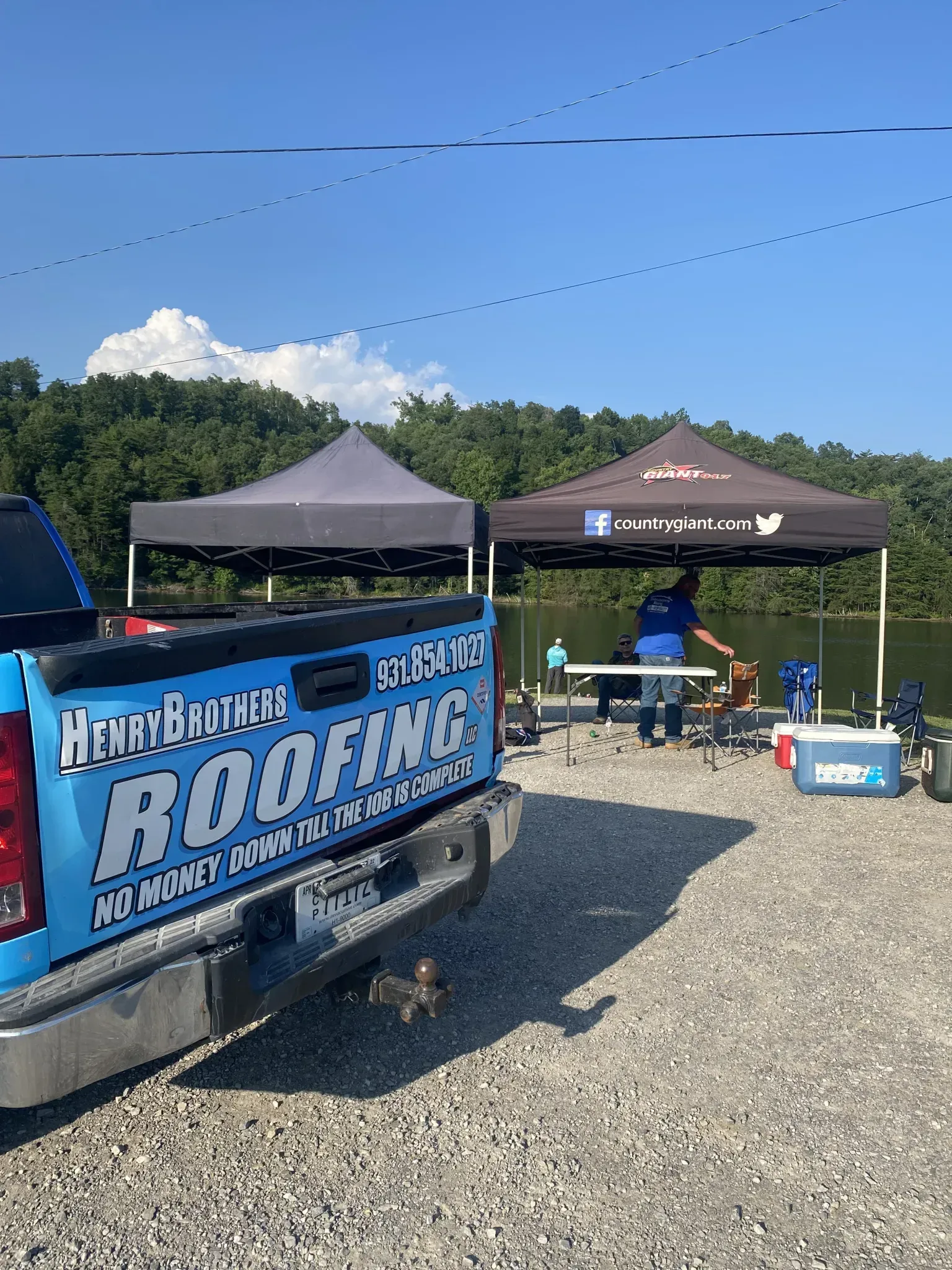 A blue truck is parked in a gravel lot next to a lake.