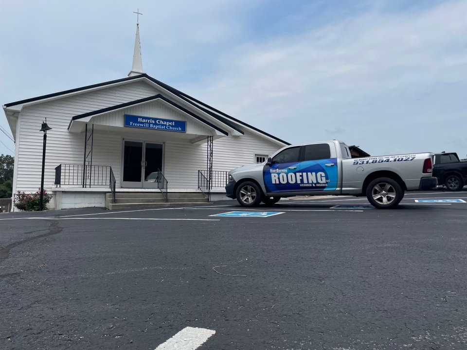 A roofing truck is parked in front of a church.