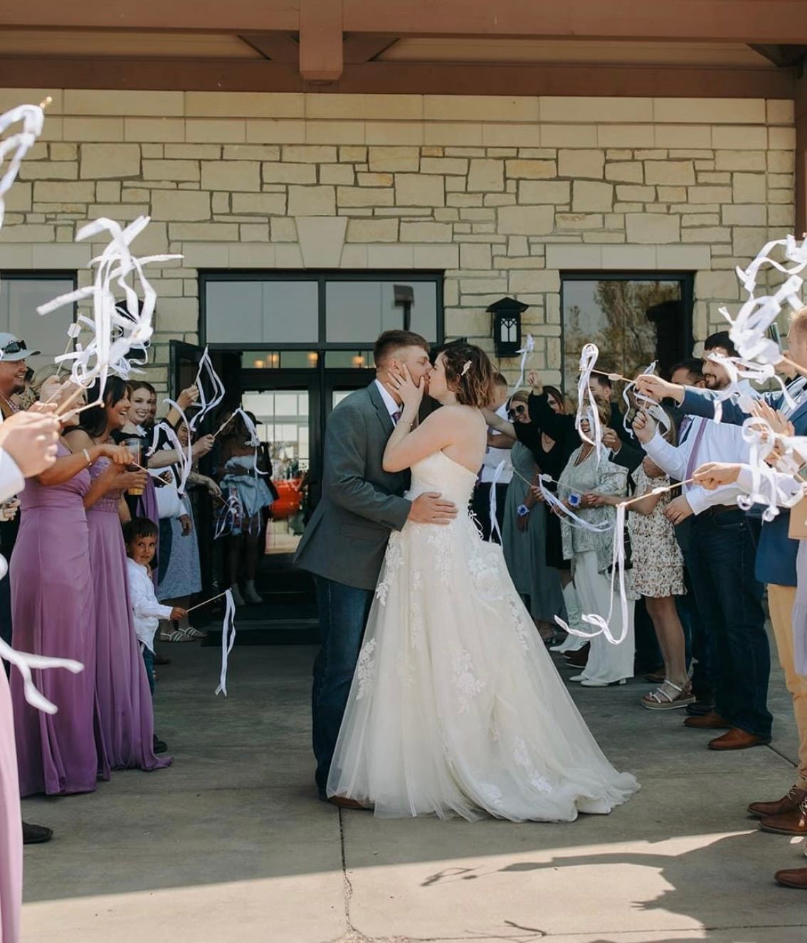 A bride and groom are kissing in front of a crowd of people holding ribbons.