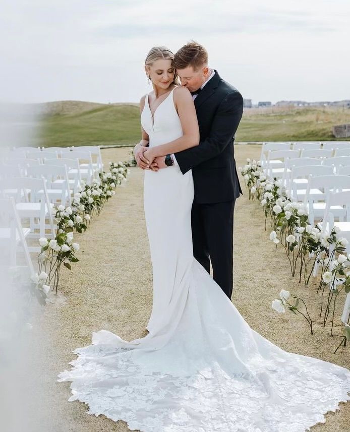 A bride and groom are standing next to each other in front of a row of white chairs.